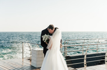 beautiful couple groom and bride are hugging on the pier against the backdrop of the sea and...