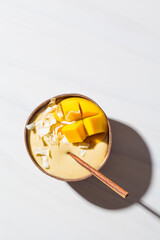 Mango smoothie bowl with coconut flakes in coconut shell, white marble background. Vegan food concept. Healthy sugar free dessert.
