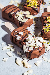 Chocolate ice cream popsicle sprinkled with almonds, coconut and pistachios, close up. Vegan ice cream in dark chocolate, top view.
