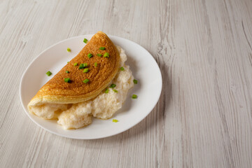 Homemade Fluffy Omelet on a white plate on a white wooden background, side view. Copy space.