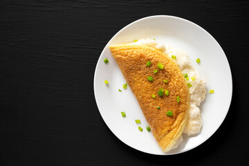 Homemade Fluffy Omelet on a white plate on a black surface, top view. Space for text.