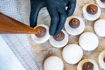 From a pastry bag, squeezes the chocolate cream onto half of the macaroons. Selective focus clouse up