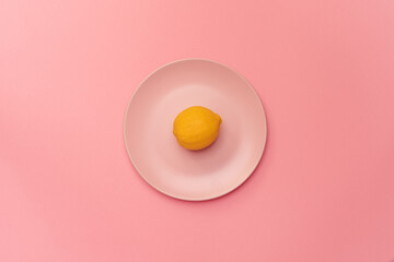 Fresh lemon on a pink plate on a pink background. The lemon in the center of the frame. Minimalism. Minimal cooking concept