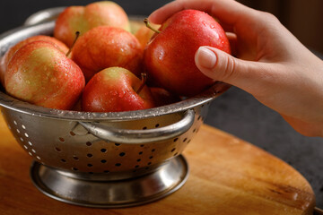 Human hand takes one apple from metallic bowl full of red ripe apples. Healthy eating. Apple pie ingridients. Cooking at home