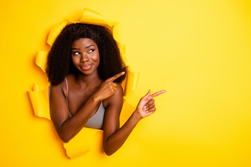 Portrait of attractive curious cheerful girl breaking paper wall demonstrating copy space isolated...