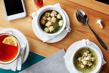 a cup of tea with lemon, a cup of soup with breadcrumbs and a telephone on a wooden table top view