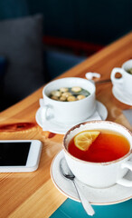 a cup of tea with lemon, a cup of soup with breadcrumbs and a telephone on a wooden table