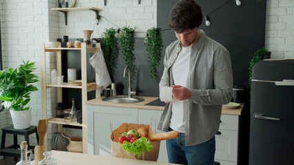 A young man with a bag of groceries checks and examines a product receipt after buying food at a...