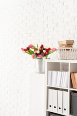Bucket of tulip flowers next to the bookshelf over white brick wall background