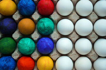 Half colored and half white eggs in square cardboard stand. Easter concept, copy space Top view