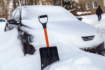 plastic snow shovel in front of snow-covered car at sunny winter morning