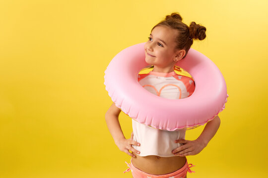 happy little child girl in swimwear with pink inflatable rubber ring on yellow background. copy space - Powered by Adobe
