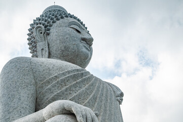 The giant statue of the Big Buddha in Phuket, made of stone, is turned three-quarters in a sitting position with a hand resting on the armrest. One of the main attractions of the resort