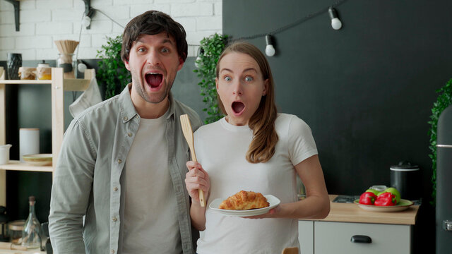 Young couple stared at the camera, standing in surprise in the kitchen at home