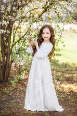 Fototapeta na wymiar little girl in a long white dress in a spring garden. A child near a flowering tree