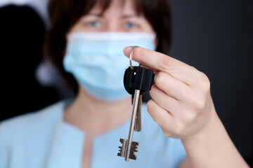 Real estate agent, apartment keys in female hands. Woman in protective face mask, concept of purchase or rental home during coronavirus pandemic