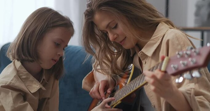 happy moments of childhood and motherhood, woman is teaching her daughter to play guitar, cheerful faces
