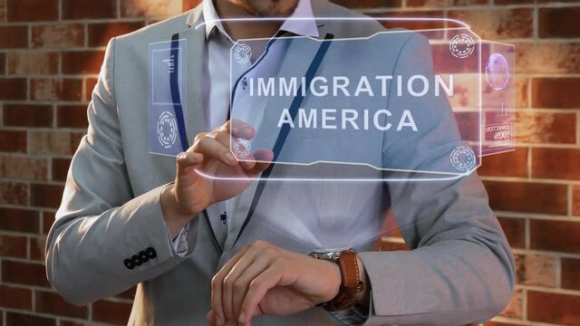 Unrecognizable businessman activates conceptual HUD holograms on smartwatch with text Immigration America. Man in jacket with holographic technology on wristwatch on background of brick wall
