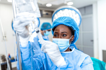 African american female Doctor in the operating room putting drugs through an IV - surgery concepts