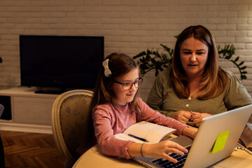 Mother and daughter follow online classes using laptop at home.