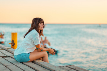 Summertime. A woman with a tattoo on her arm, sitting relaxed on the pier by the sea. Side view. Copy space