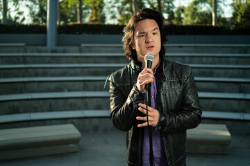 Thoughtful Wondering or Depressed Male Asian Stand Up Comedian with Microphone in Empty Auditorium...