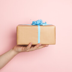 Hand holding gift with blue ribbon on pink card background