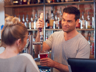 Smiling Male Bartender Behind Counter Serving Female Customer With Beer