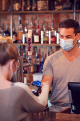 Female Customer Wearing Mask In Bar Making Contactless Payment For Drinks During Health Pandemic