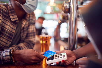Male Customer Wearing Mask In Bar Making Contactless Payment For Drinks During Health Pandemic
