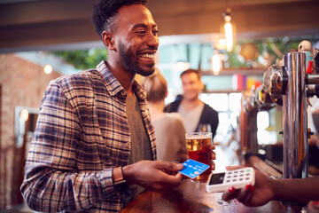 Smiling Male Customer In Bar Making Contactless Payment With Card For Drinks To Female Bartender