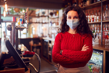 Portrait Of Female Bar Worker Wearing Face Mask During Health Pandemic Standing Behind Counter