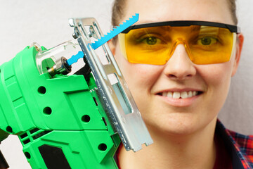 portrait of a worker with a jigsaw. a woman in safety glasses holding an electric jigsaw.