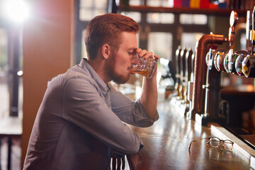 Unhappy Man Sitting At Pub Bar Drinking Alone With Glass Of Whisky