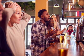 Group Of Disappointed Customers In Sports Bar Watching Sporting Event On Television