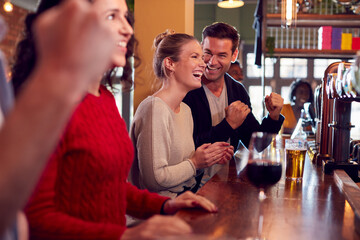 Group Of Excited Customers In Sports Bar Watching Sporting Event On Television