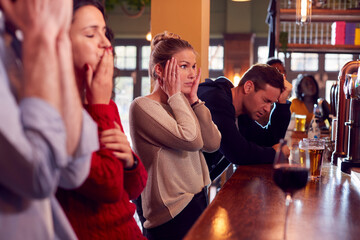 Group Of Disappointed Customers In Sports Bar Watching Sporting Event On Television