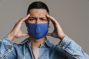 Unhappy guy with headache posing in medicine protective mask