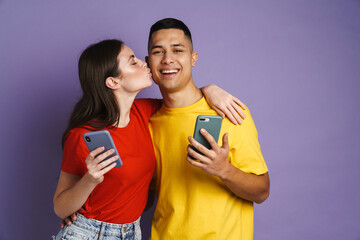 Naklejka premium Happy beautiful couple kissing while using mobile phones