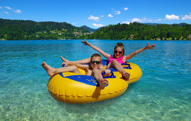 Boy and girl on inflatable float in lake. Little children floating in yellow raft on surface water.