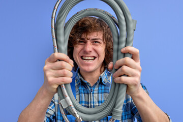 young plumber man holding hose and looking at camera through it, strong confident sanitary engineer...
