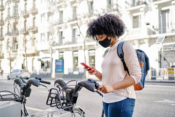 African-American woman using her smart phone to pay for a bicycle rental. Eco-friendly transportation concept