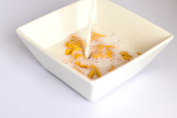 Milk being poured in to the white bowl with cereal in it. Food