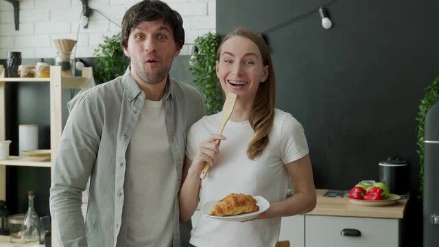 Young couple stared at the camera, standing in surprise in the kitchen at home