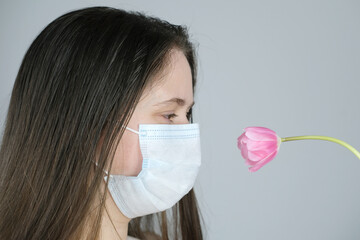 young woman, a girl in a white medical mask with long blond hair holds one pink tulip near her...