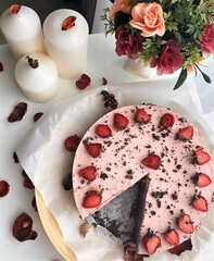 Strawberry cheesecake with flowers and candles on the white table