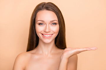 Portrait of charming cheerful girl holding on palm copy space facial therapy isolated over beige pastel color background