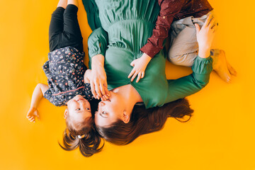 Obraz premium Happy mom with children lie on yellow background. Spending time with children.