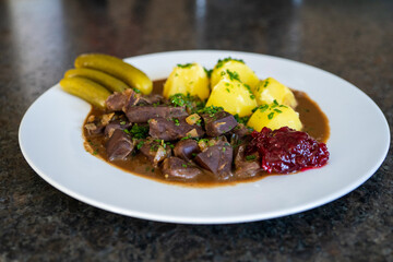 ready to eat - roasted heart, kidneys and liver from a red deer calf with potatoes, sauce, pickles and cranberries