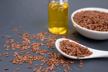 Flax seeds with a bottle of flaxseed oil behind on gray background with copy space - healthy eating, dieting or skin care concept. Top benefits of linseed in medicine and cosmetology. Selective focus